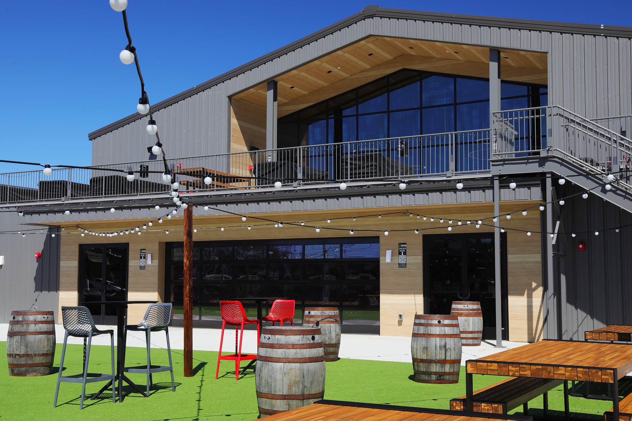 The Beer Garden with barrel tables, high tops, picnic tables and string lights outside the hall